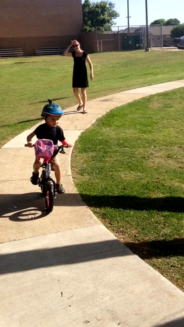 Video thumbnail showing: A boy rides a bicycle down a sidewalk alongside a pond. His mother yells at him to turn and he swerves into the water.