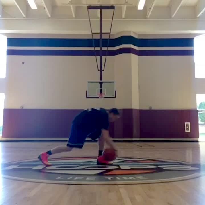 Video thumbnail showing: A teen boy picks a basketball up, then throws it behind his back into a hoop in a gymnasium.